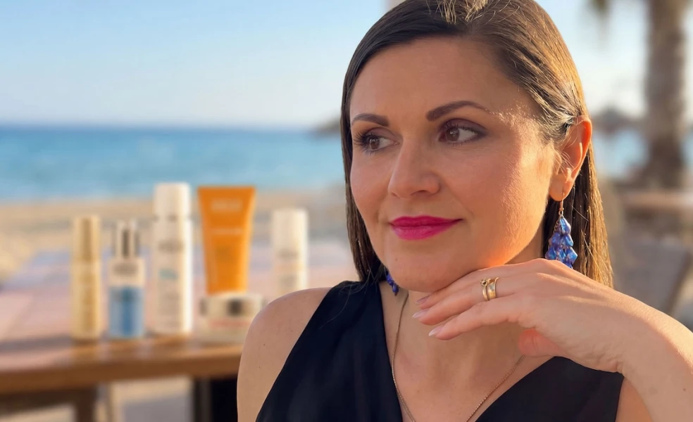 Henrieta Martinková, CEO značky ANNEMARIE BÖRLIND pre Slovensko a Česko, na pláži pri mori s opaľovacou kozmetikou na stole v pozadí